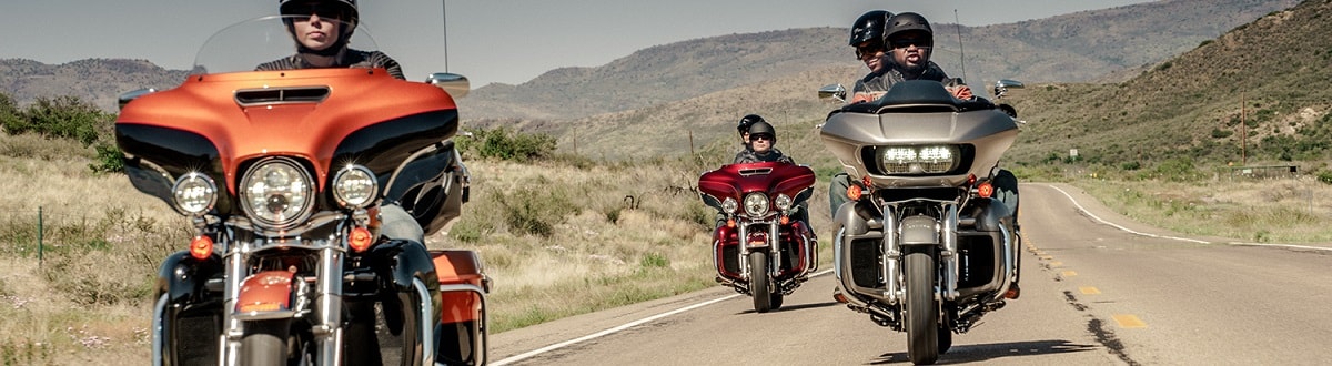 Three people riding Harley-Davidson® motorcycles down the open country road with hills 